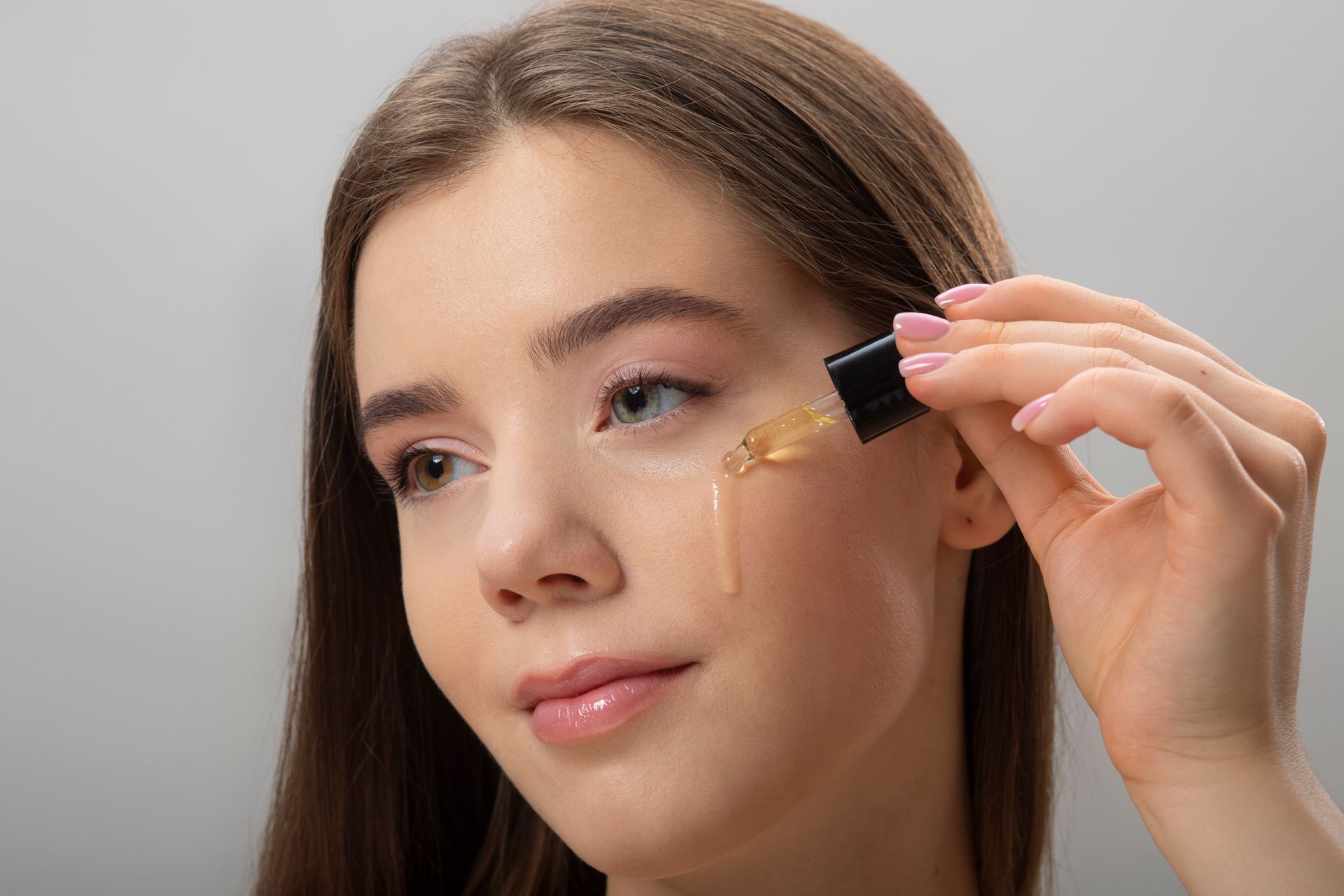 A woman is applying a serum to her face with a pipette.
