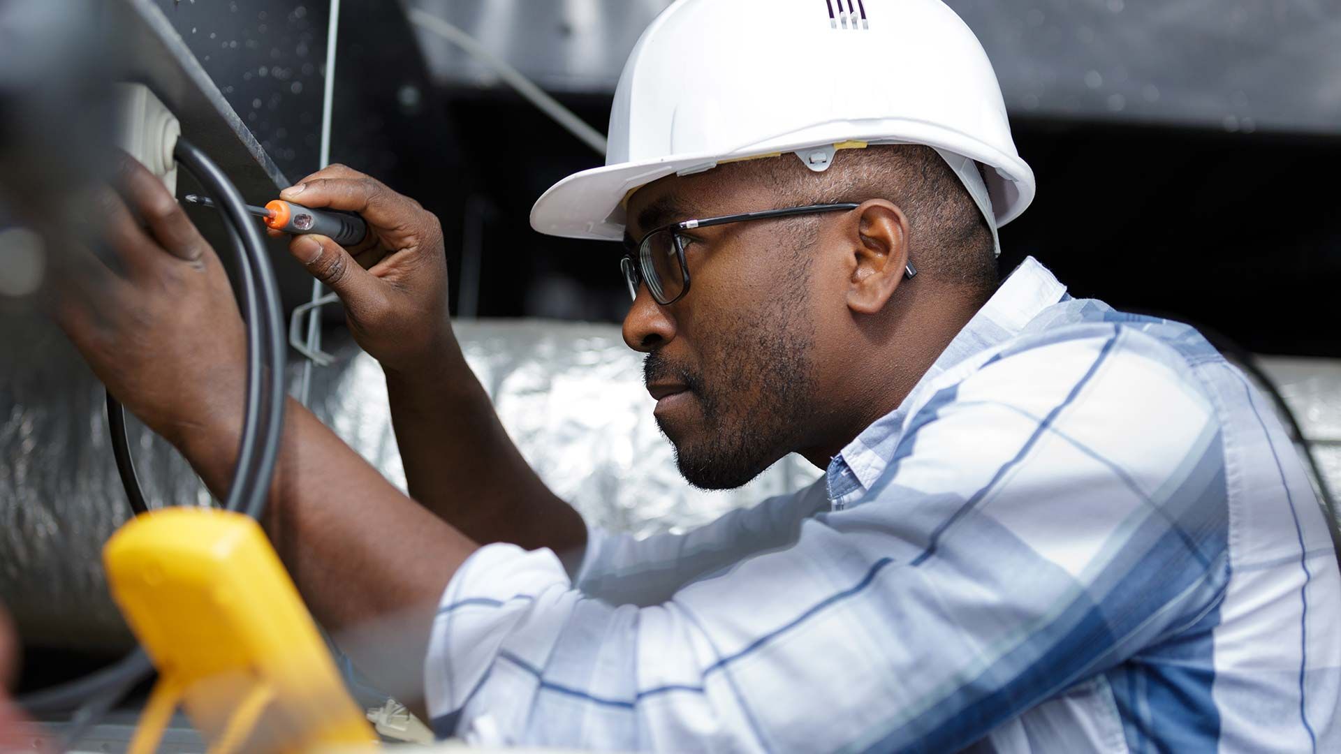 A man wearing a hard hat is working on a pipe.
