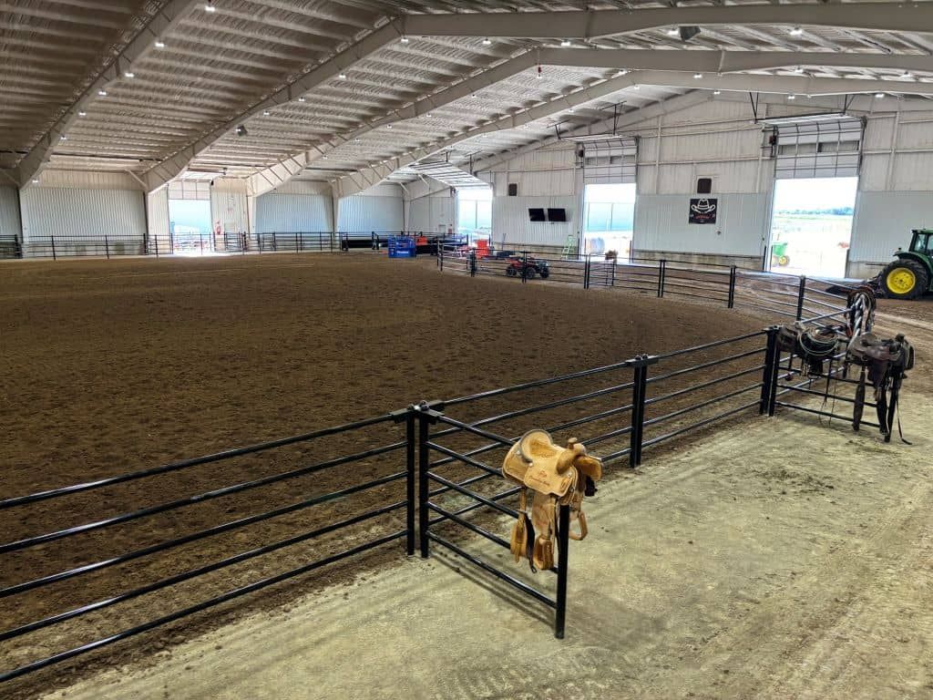 A large indoor arena with a fence and a tractor in the background.