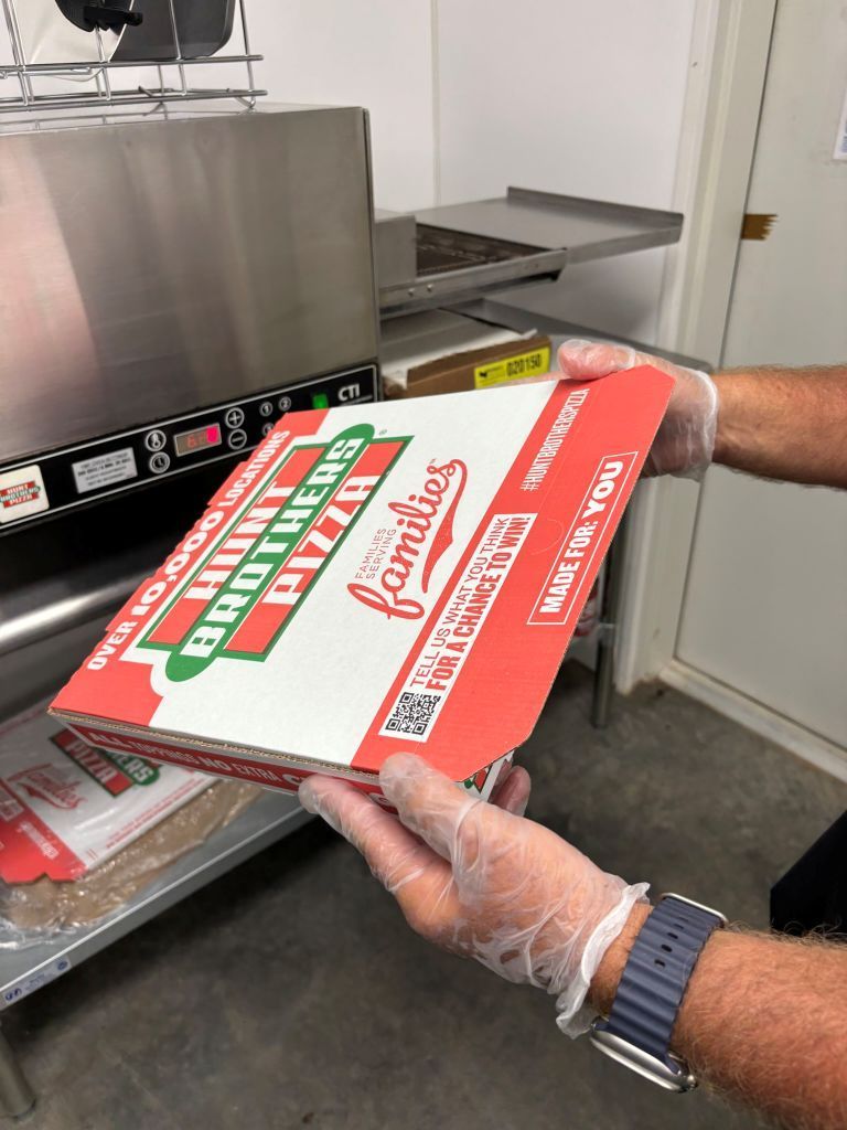 A person wearing gloves is holding a box of pizza