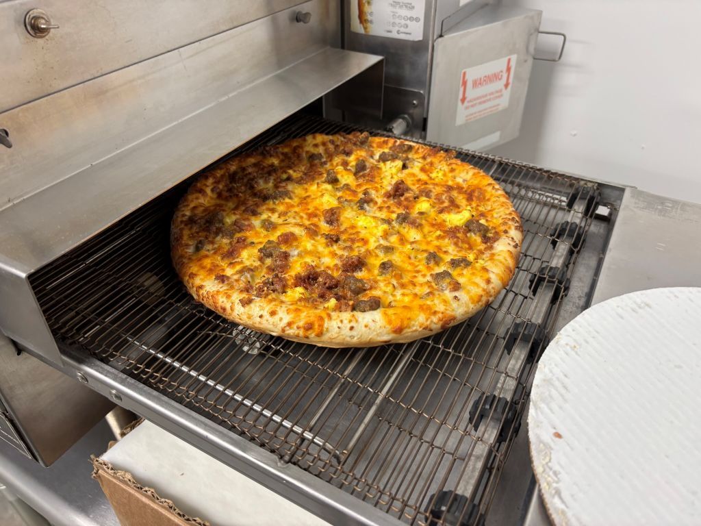 A pizza is being cooked in a conveyor belt oven.