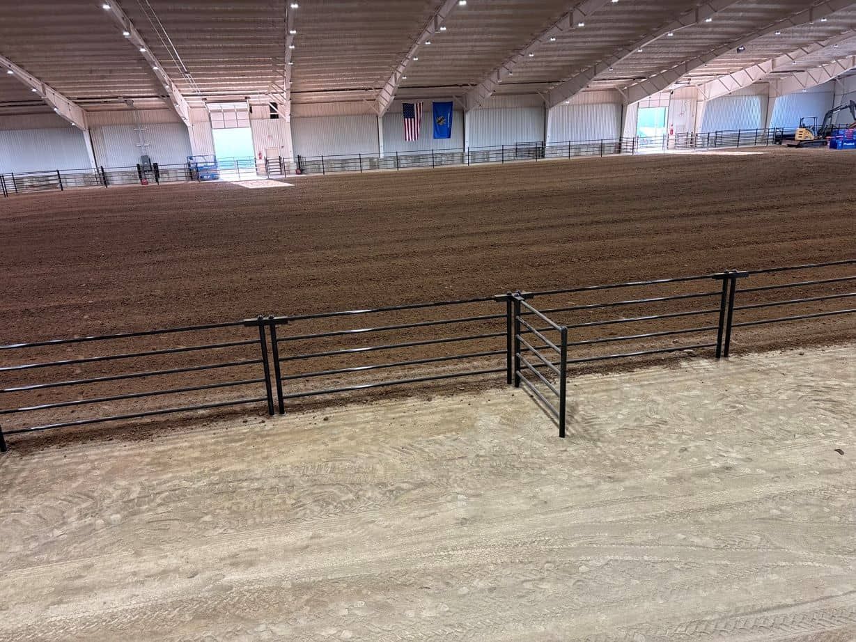 A large indoor arena filled with dirt and a fence.