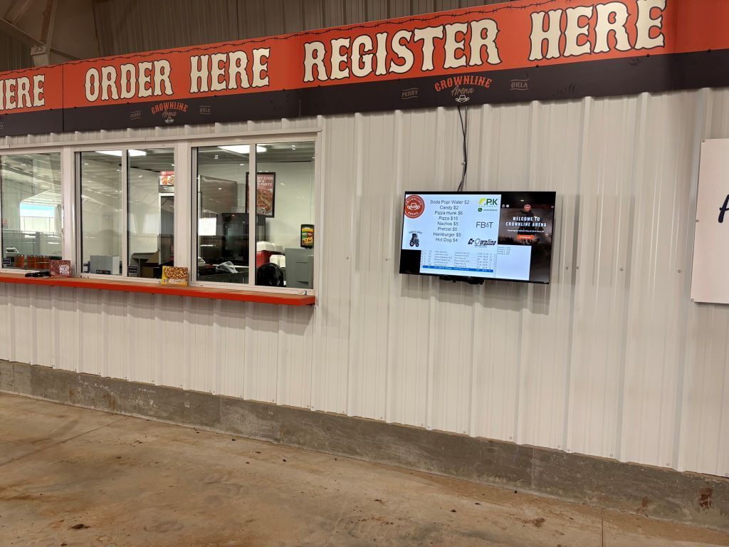 Concessions stand window with a menu displayed on a mounted television. The sign above says 