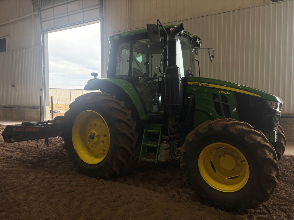 A green and yellow john deere tractor is parked in a warehouse.