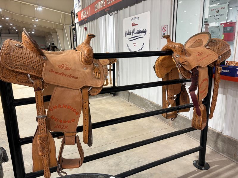 Two brown leather western saddles on a black metal rack inside a building.