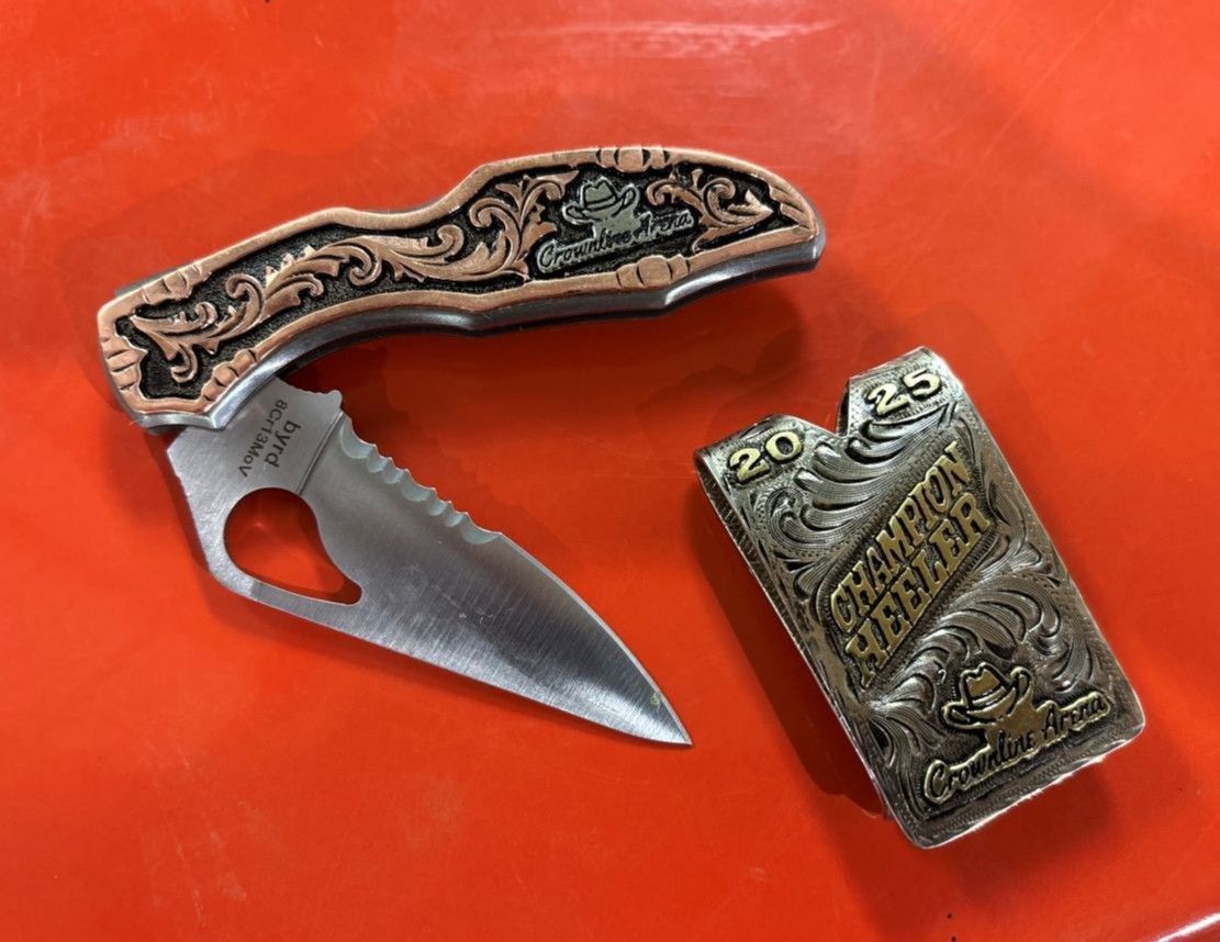 A decorative pocket knife and a matching lighter with ornate designs and engraved lettering sit on a red surface.