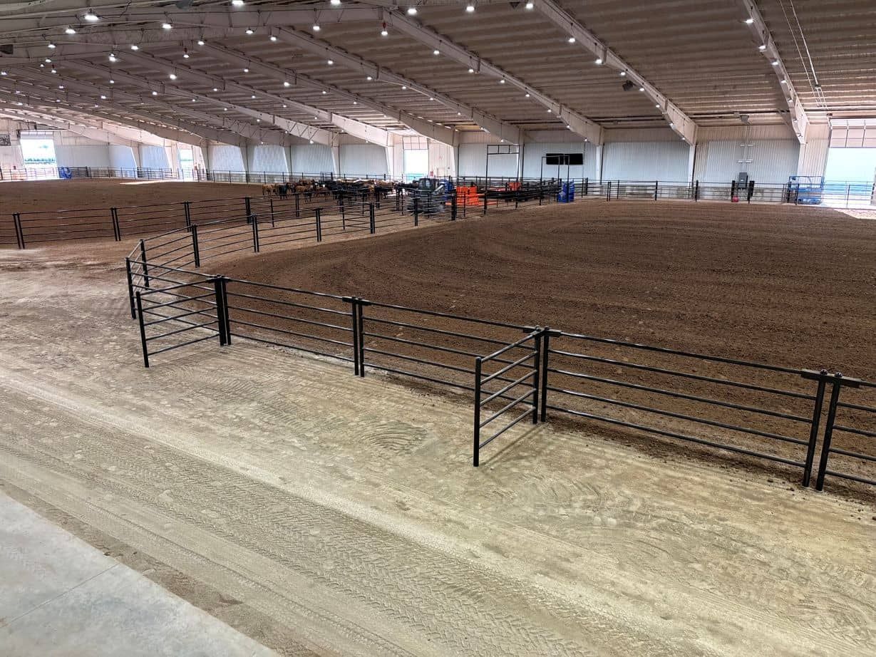 A large indoor arena filled with dirt and a fence.