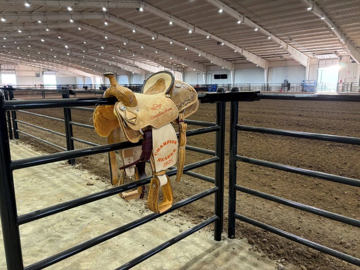 A saddle is hanging on a fence in an arena.