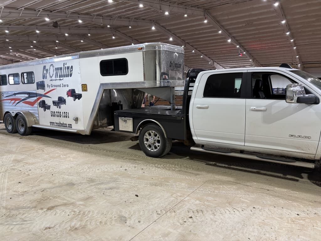 A white truck is towing a horse trailer in an arena.