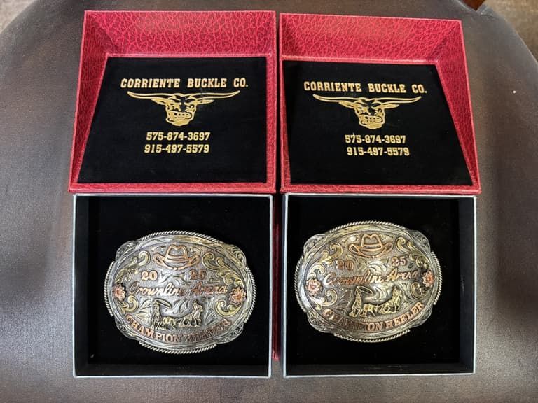 Two championship belt buckles in red boxes that say corriente buckle co