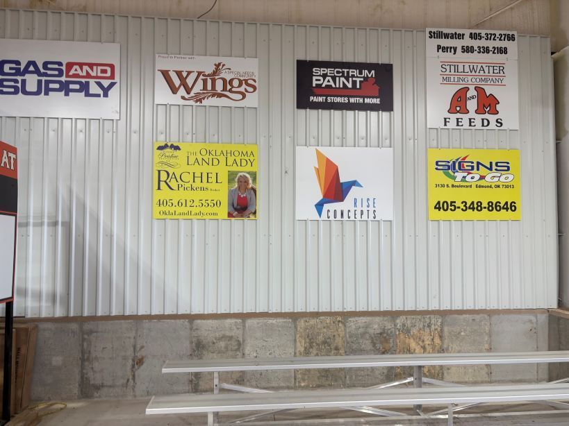 Signs on a corrugated metal wall. Businesses include Gas and Supply, Wings, and Signs.