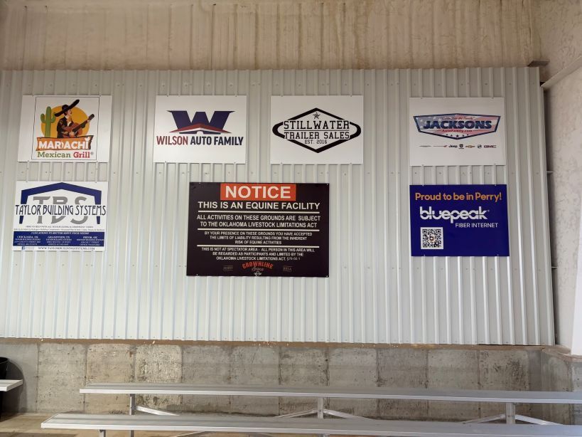 Signs on a corrugated metal wall. Includes company logos and a notice about the facility.