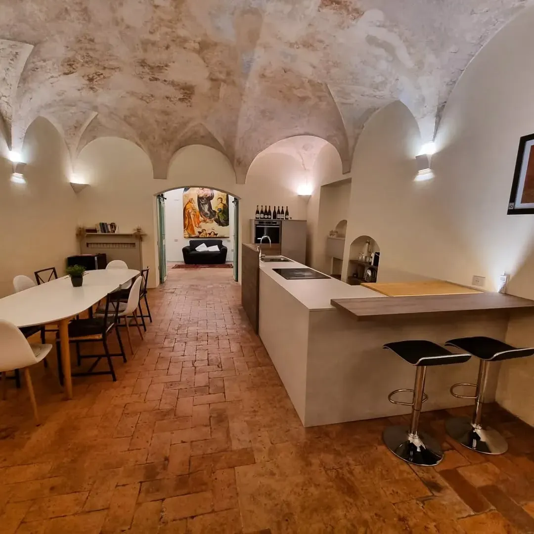 Stanza lunga e arcuata con isola cucina, tavolo da pranzo e porta che conduce a una zona salotto.