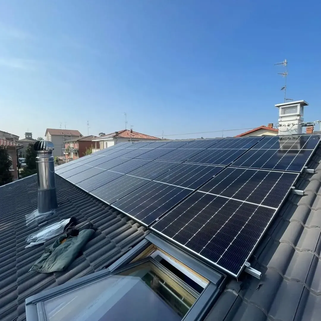 Pannelli solari installati su un tetto di tegole sotto un cielo azzurro, con edifici circostanti.