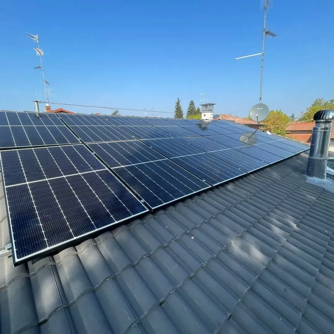 Pannelli solari su un tetto di tegole con antenne contro un cielo azzurro e terso.