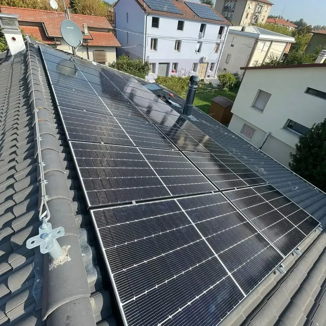 Pannelli solari installati su un tetto di tegole, con un'antenna parabolica e edifici urbani sullo sfondo.