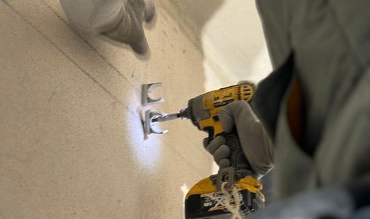 Persona che utilizza un trapano giallo per avvitare le staffe a un muro, primo piano.