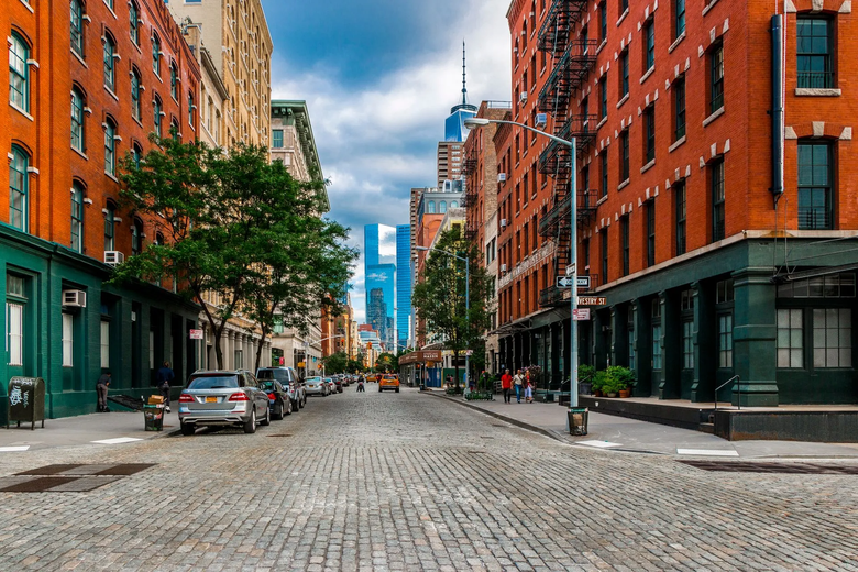 A cobblestone street in a city with a lot of buildings and cars parked on the side of it.