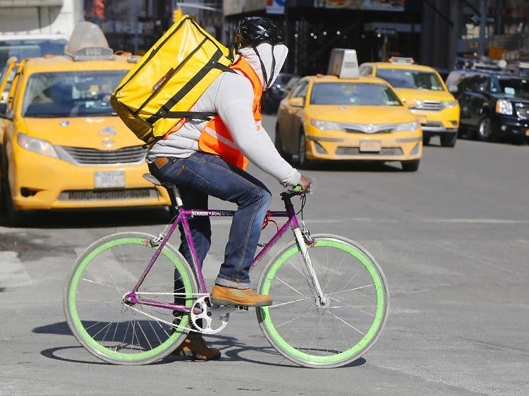 A man is riding a bike with a yellow bag on his back.