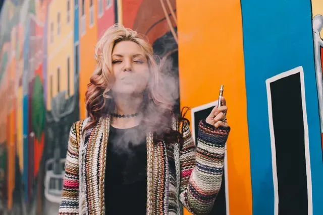 woman holding vaporizer in front of colorful mural