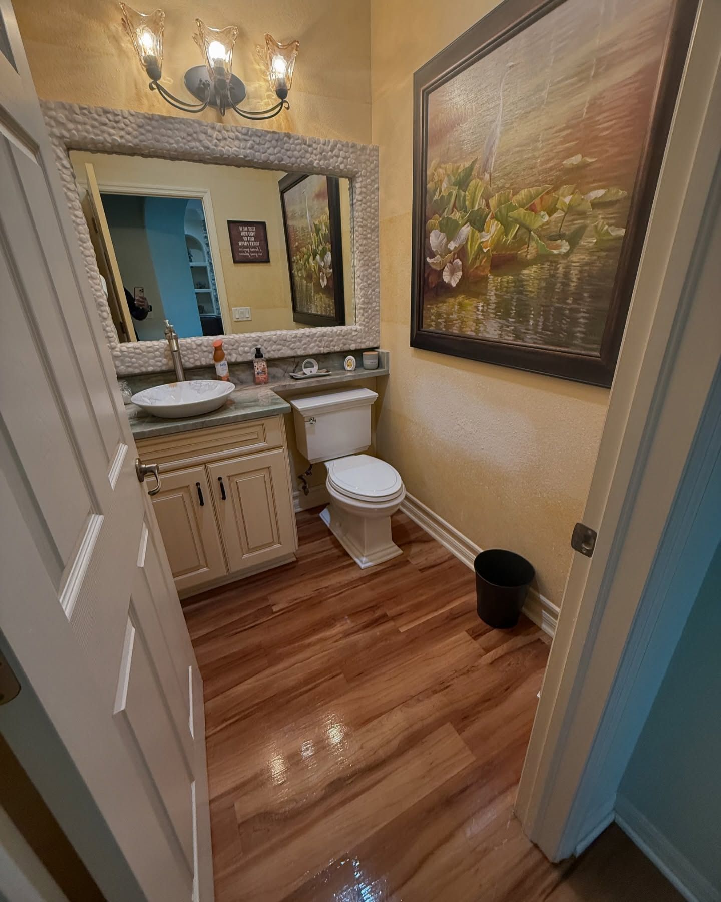 A bathroom with a toilet , sink , mirror and picture on the wall.
