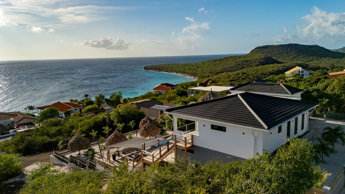 Uitzicht op de oceaan met witte huizen, groene bomen en blauw water onder een gedeeltelijk bewolkte hemel.