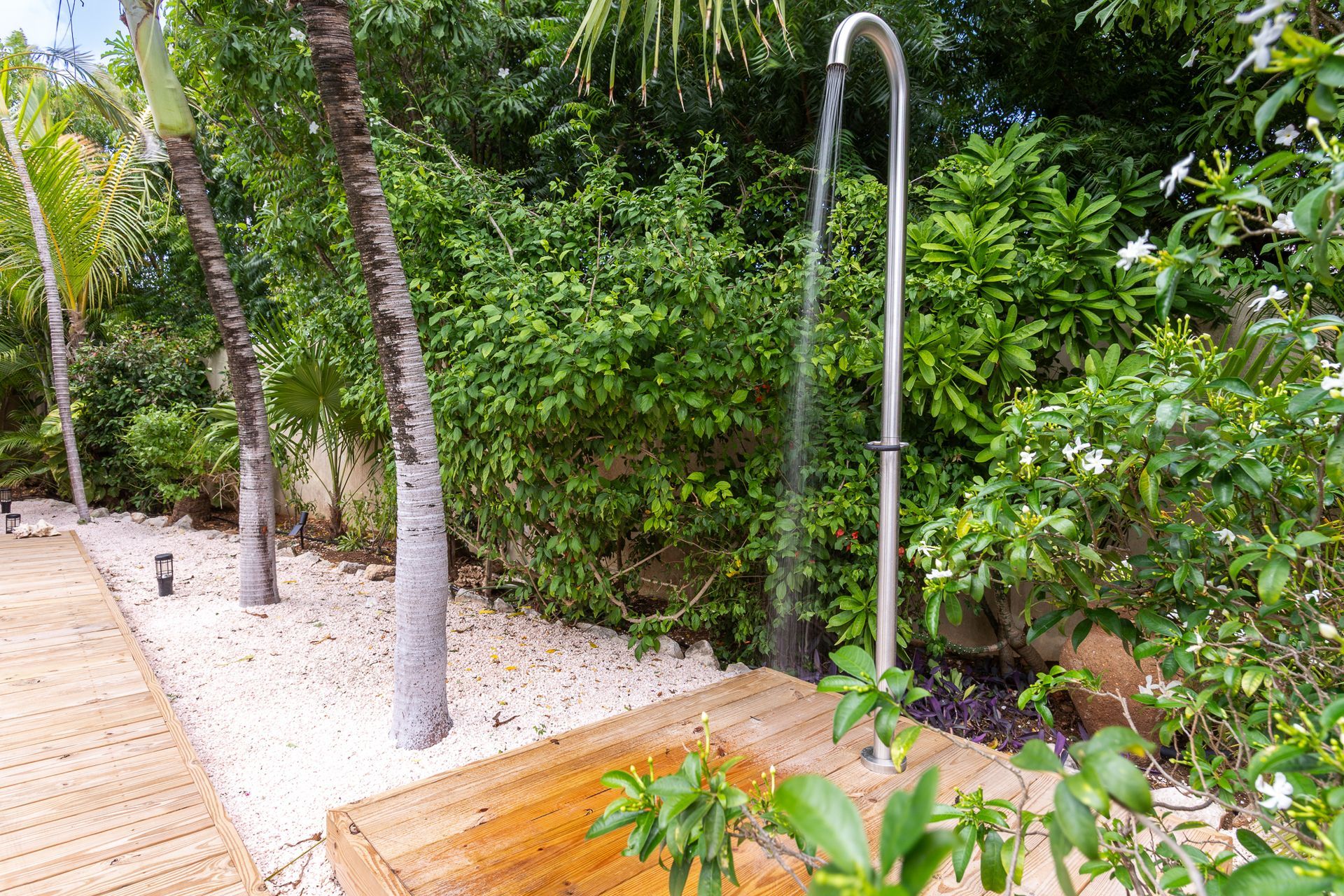 Buitendouche in een tropische tuin met houten vlonder en stenen pad.