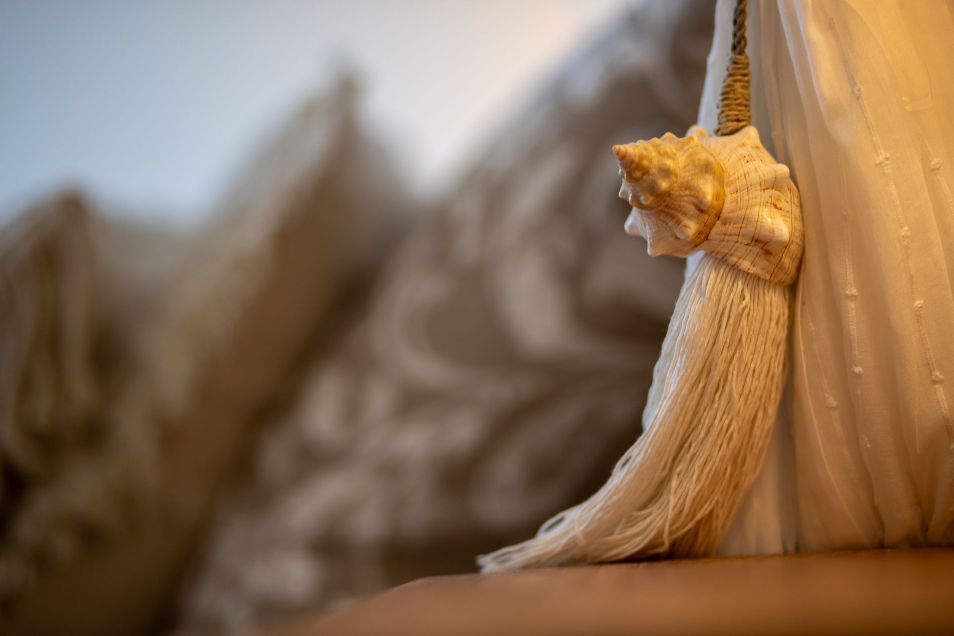 Close-up van een witte kwast met schelpdetails, hangend tegen een gedrapeerde stof en een wazige achtergrond.