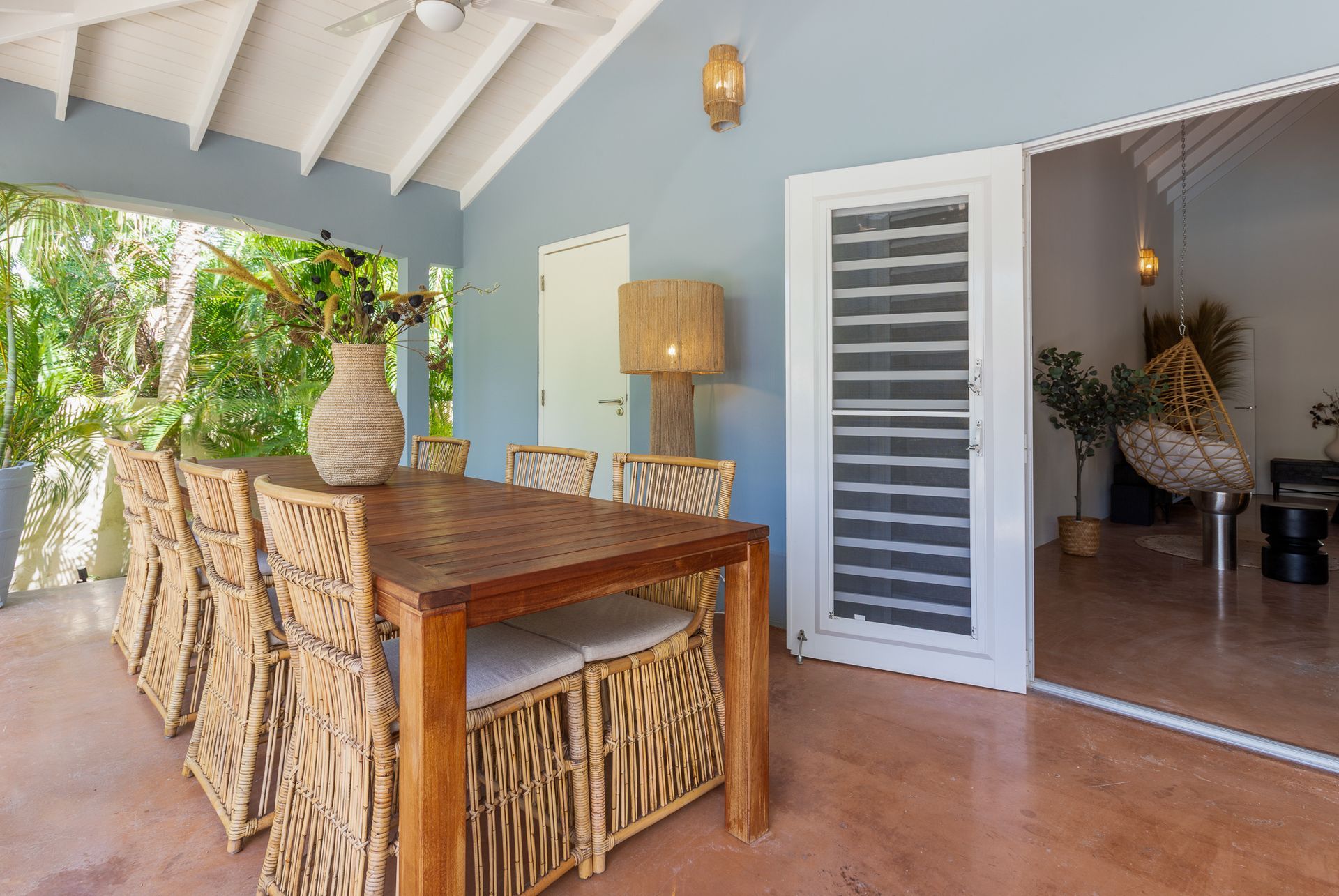 Overdekt terras met eettafel en stoelen, grenzend aan een kamer met decoratieve elementen.