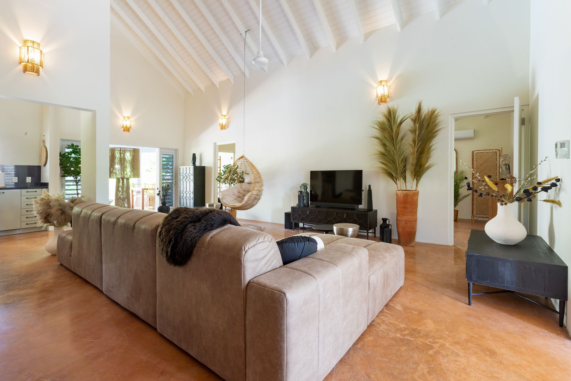 Ruime woonkamer met beige hoekbank, tv en hoge plafonds.