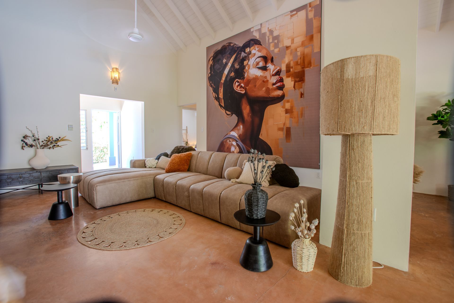 Woonkamer met beige hoekbank, groot kunstwerk en een geweven vloerlamp.