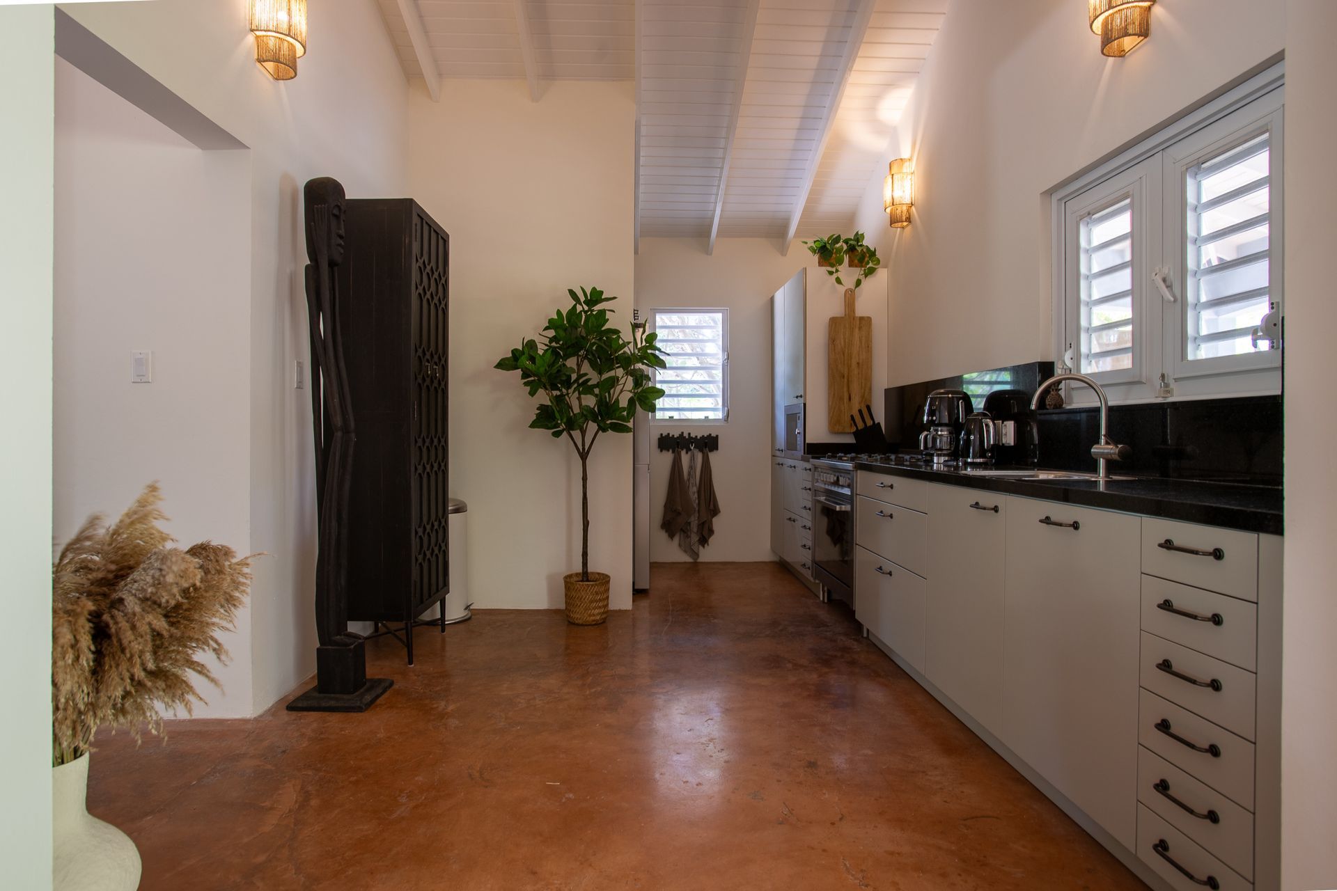 Keuken met witte kasten, donker aanrechtblad, bruine vloer en een hoge zwarte kast.