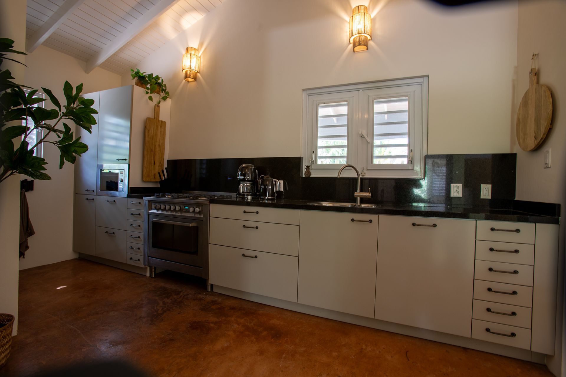 Keuken met witte kasten, zwarte werkbladen, roestvrijstalen apparaten en wandverlichting.