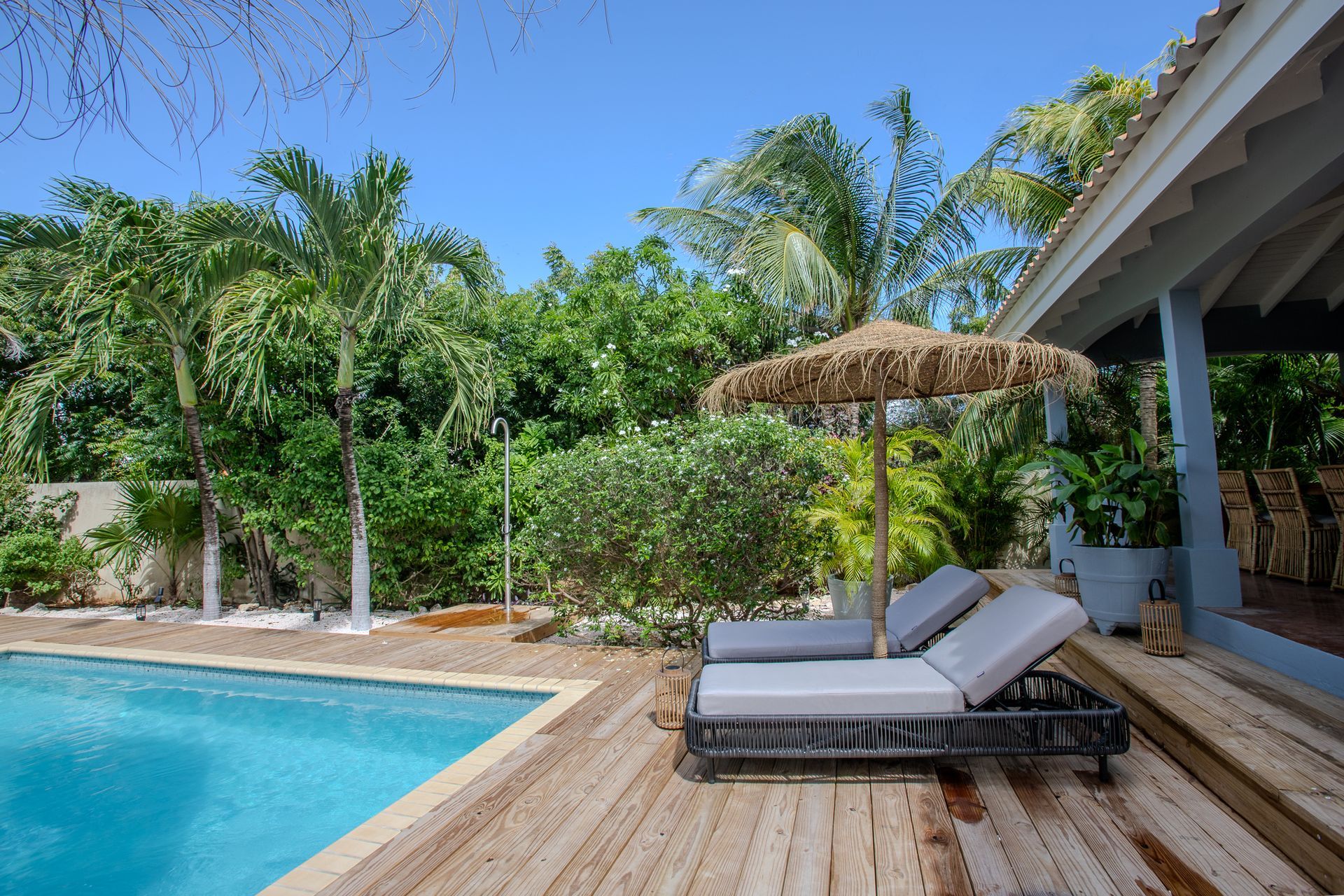 Een tafereel bij het zwembad met ligstoelen onder een rieten parasol, een houten terras 