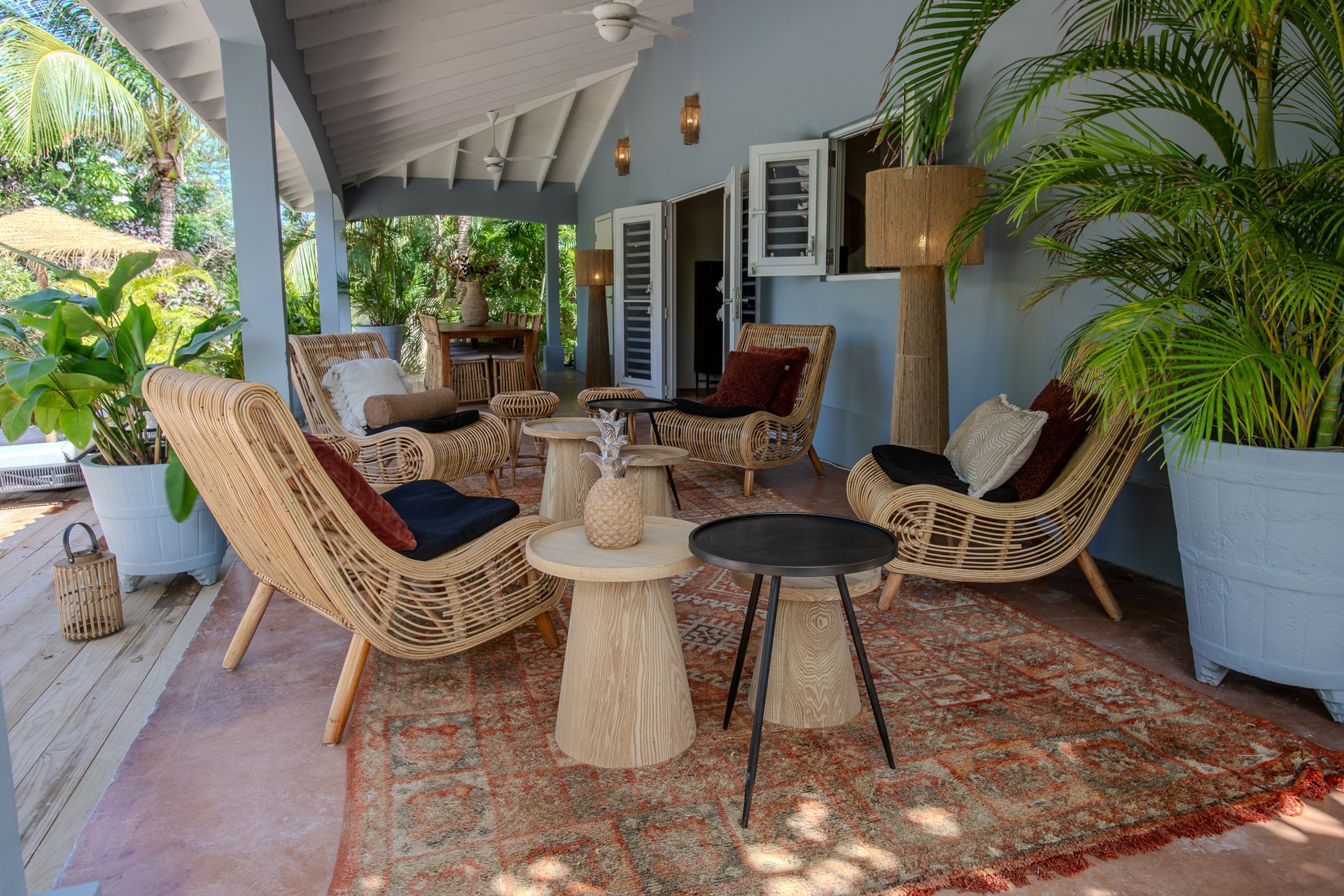 Buitenpatio met gevlochten stoelen, vloerkleden en bijzettafels onder een overdekte veranda.