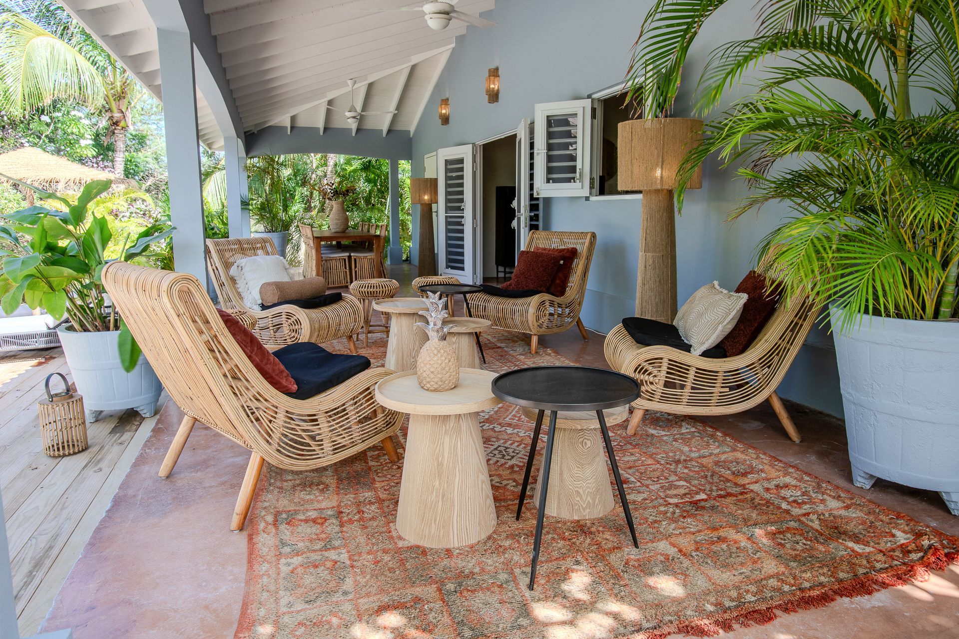 Buiten zitgedeelte met rieten stoelen, een vloerkleed en potplanten.