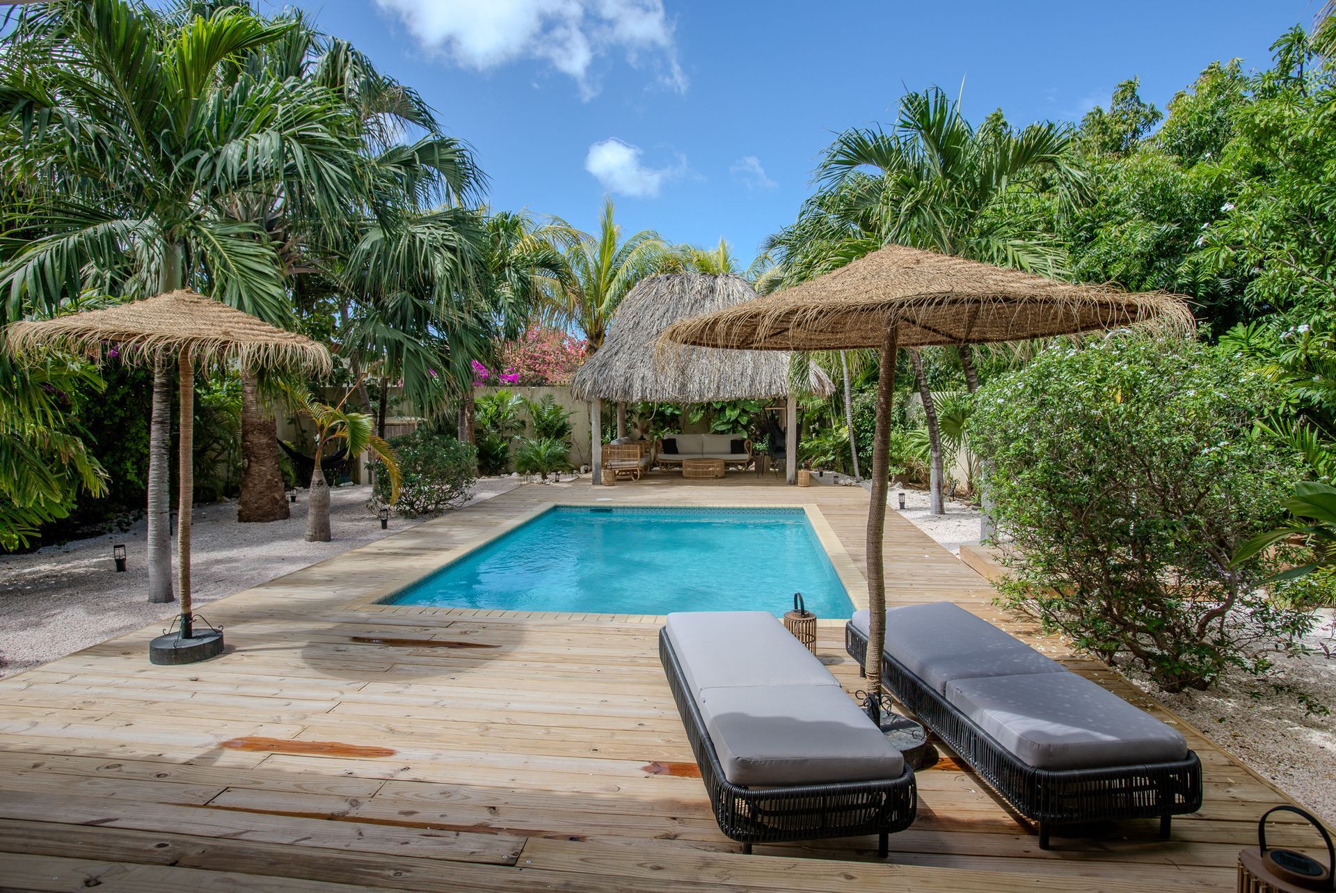 Zwembad met rieten parasols, ligstoelen en tropische beplanting.