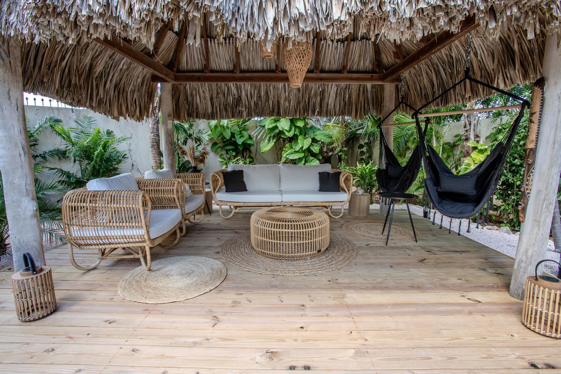 Rotanmeubilair onder een prieel met een rieten dak. Inclusief een bank, stoelen, een salontafel en een hangstoel. 