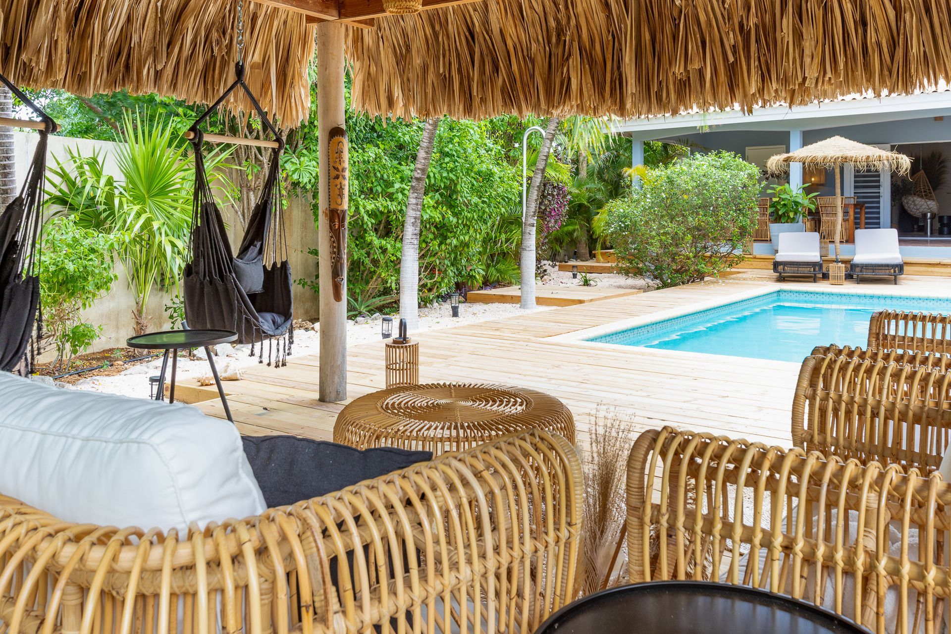 Een ontspannende buitenruimte met zwembad, rieten meubels en een rieten dak.