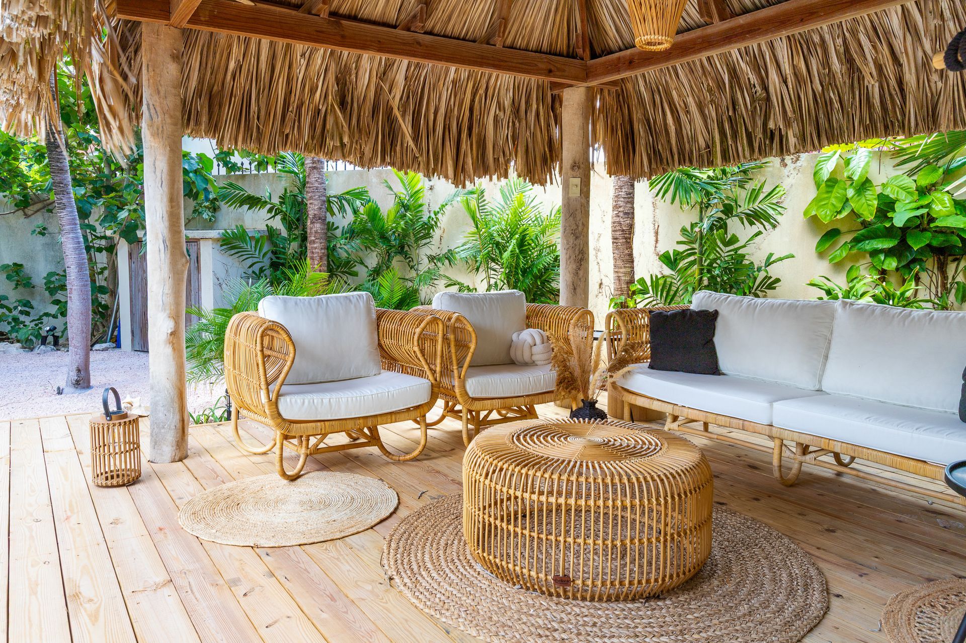 Een zitgedeelte buiten onder een rieten dak met rieten meubels en witte kussens.