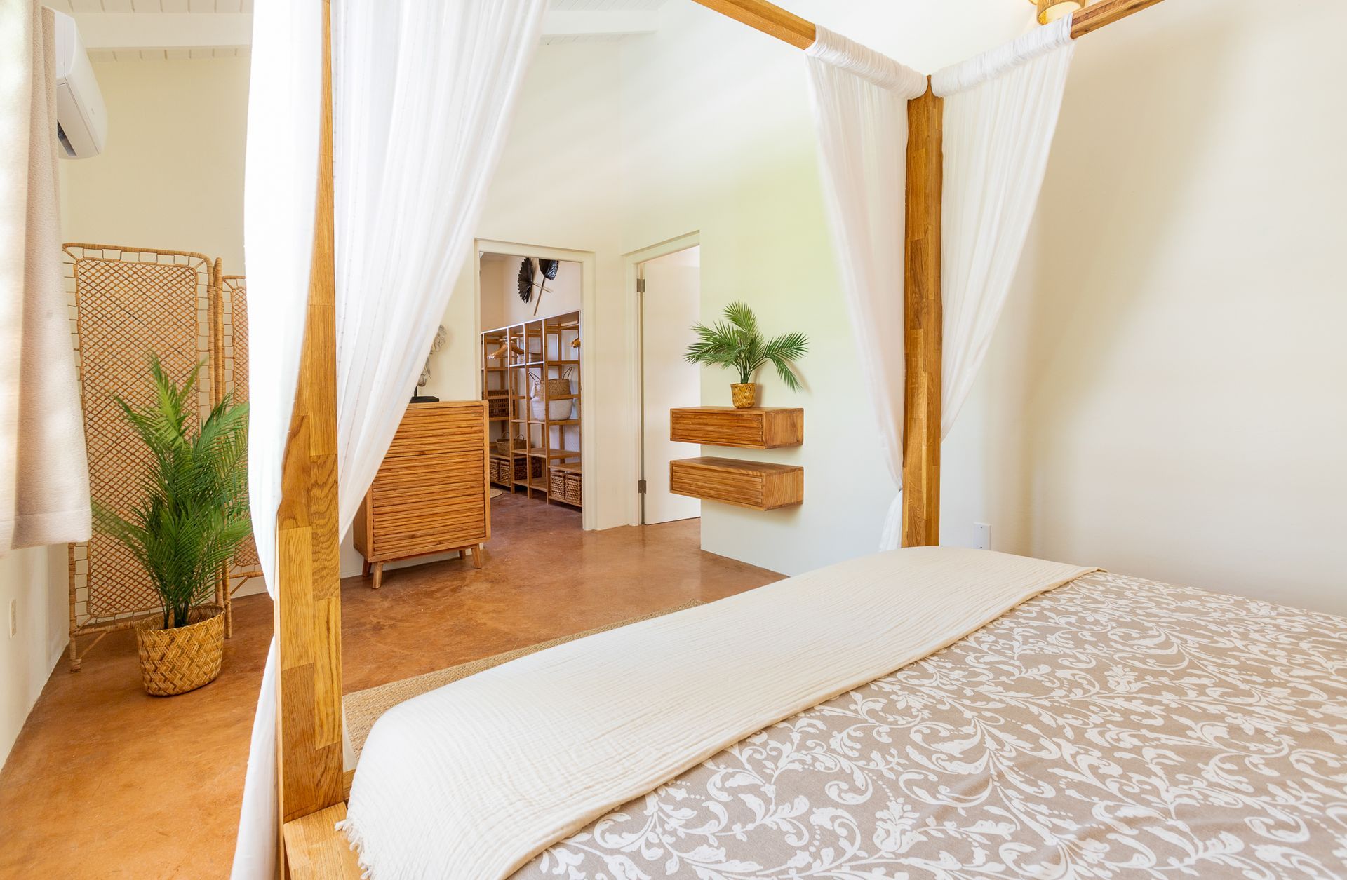 Slaapkamer met hemelbed en transparante gordijnen. Houten accenten en planten in een lichte, witte kamer.