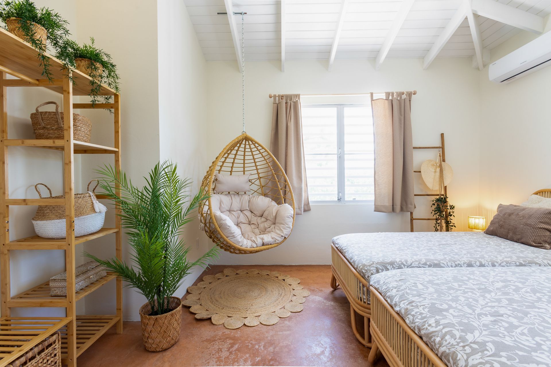 Slaapkamer met twee bedden, een hangstoel en houten planken, met planten en neutrale tinten.