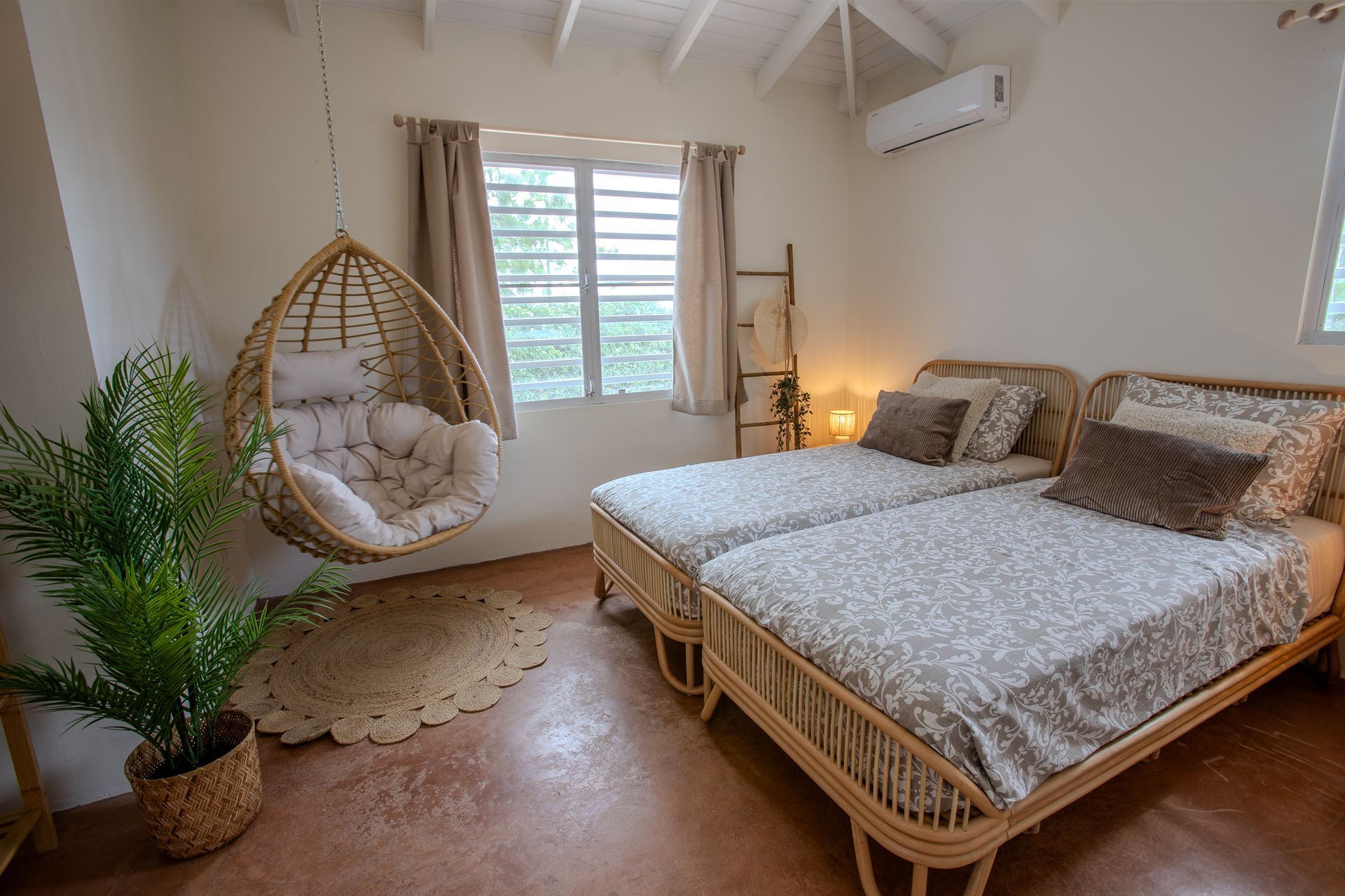 Slaapkamer met twee eenpersoonsbedden, een hangstoel, een raam en een potplant.