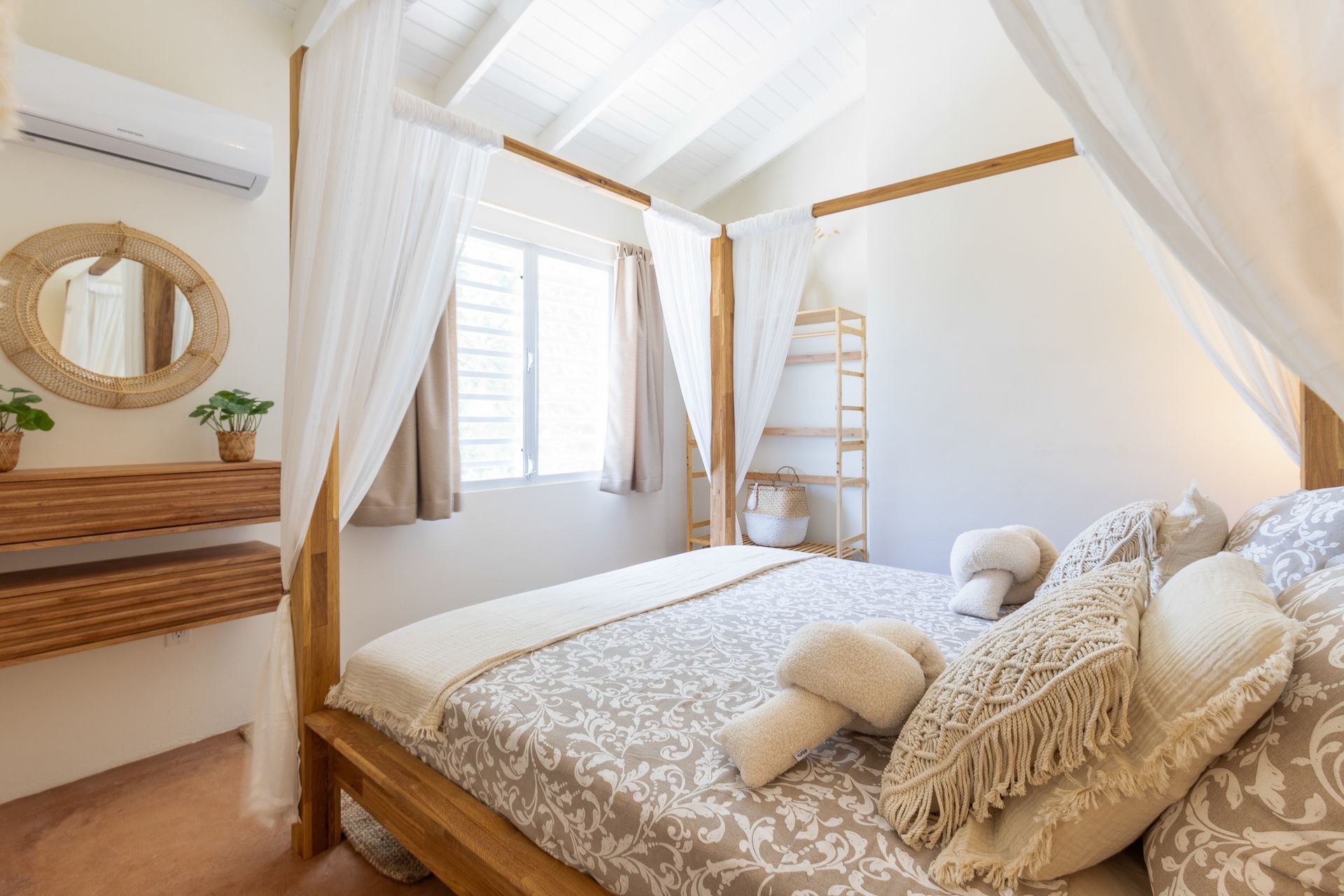 Slaapkamer met hemelbed, wit beddengoed, houten accenten en een ronde spiegel.