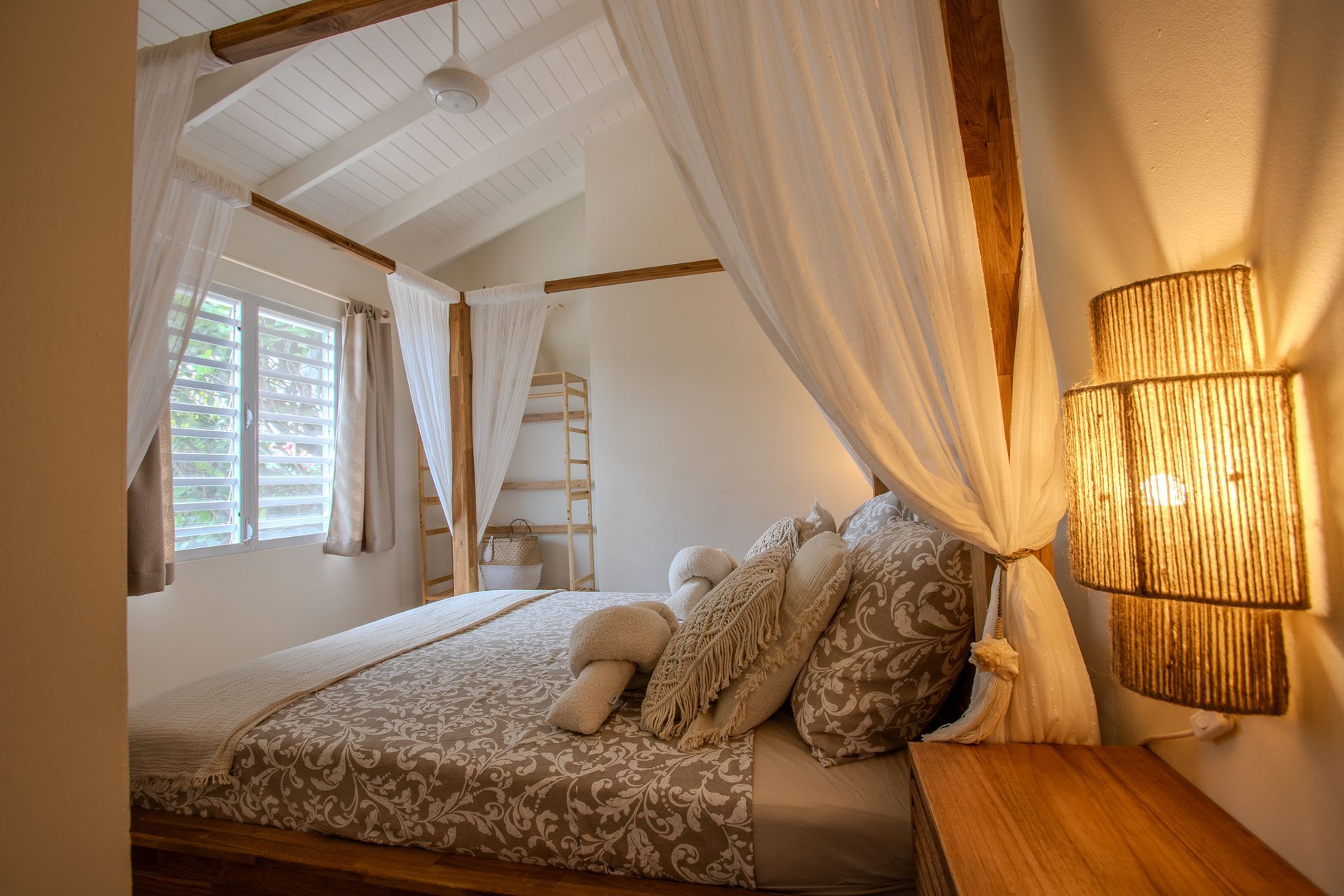 Slaapkamer met hemelbed, witte gordijnen, houten accenten en decoratieve wandlamp.