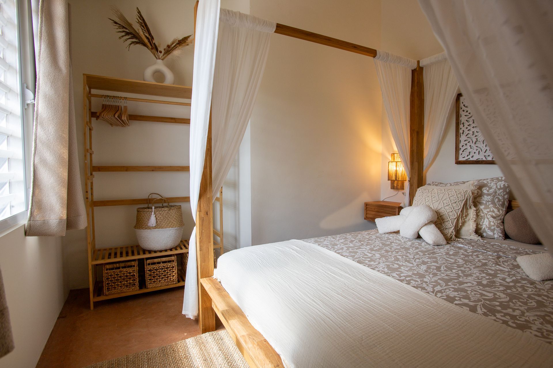 Slaapkamer met hemelbed, neutrale tinten, houten plank met decoratie en raam.