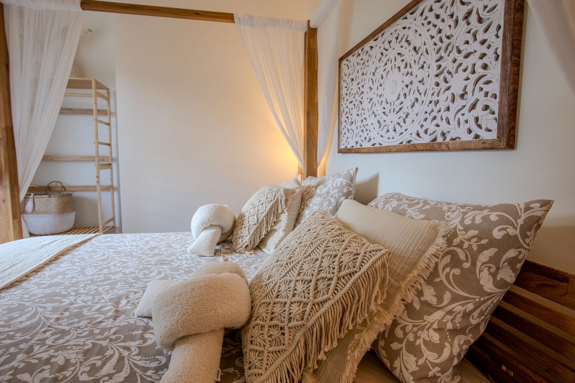 Slaapkamer met bed, kussens, dekbed met patroon, decoratief hoofdbord, gordijnen en boekenplank.