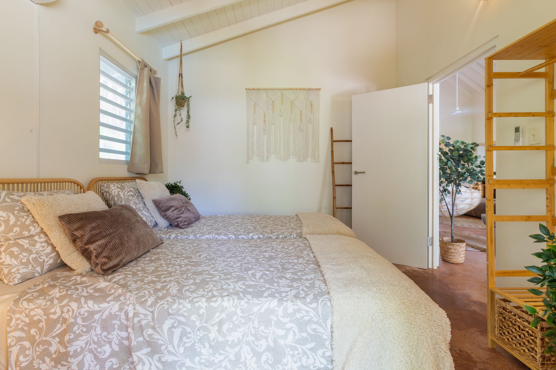 Gezellige slaapkamer met bed, kussens en een doorgang naar een andere kamer. Witte muren, houten accenten, natuurlijk licht.