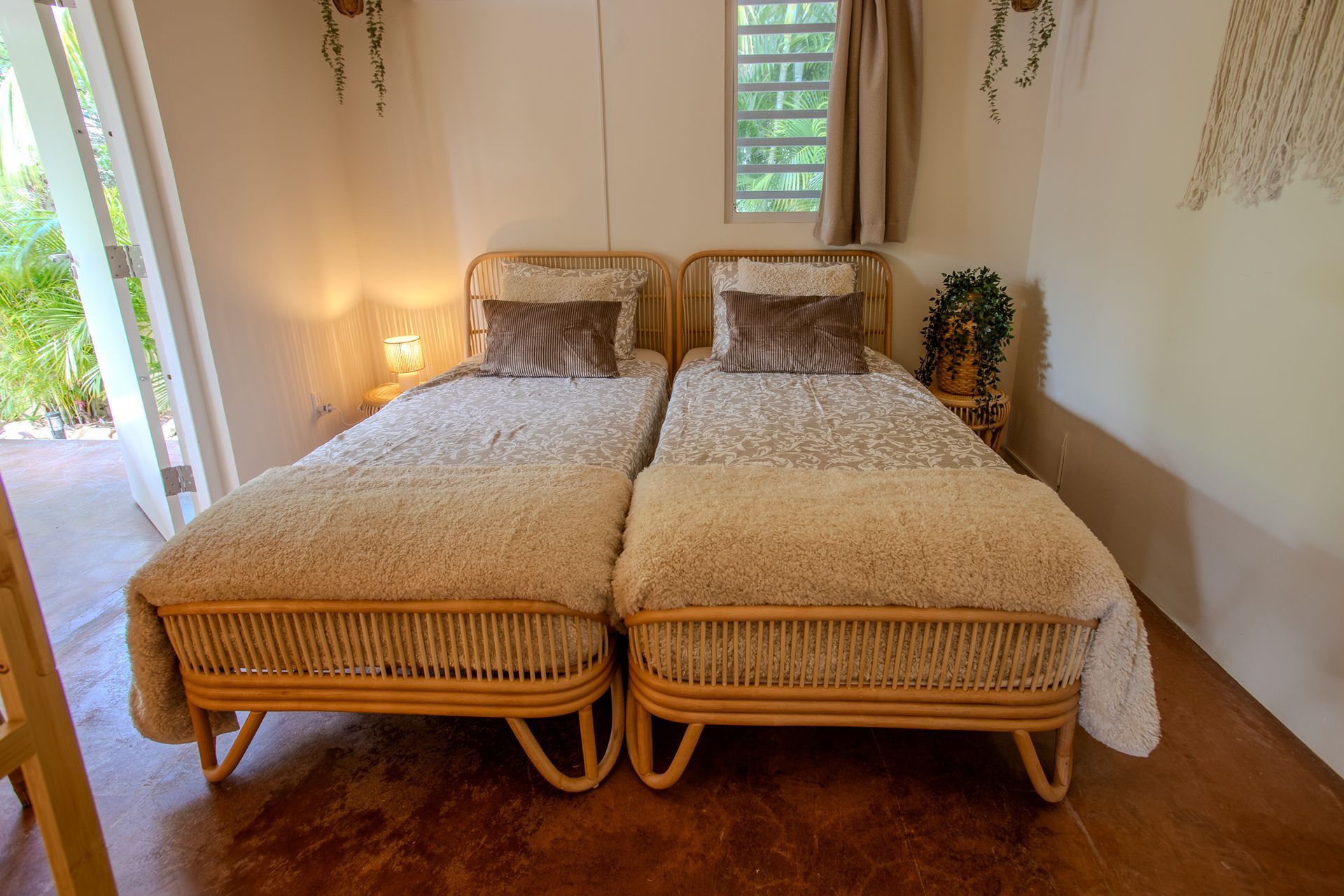 Twee eenpersoonsbedden met rotan frames in een slaapkamer met een open deur en een raam.