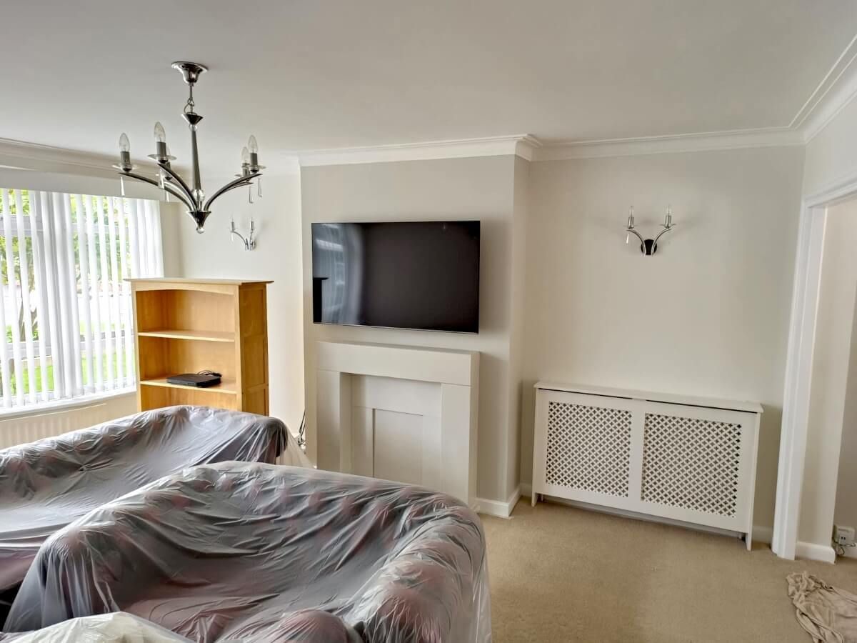 Sunderland living room with white walls, a mounted TV over a fireplace, two covered sofas, and a radiator. Painted by Foxglove Decor.